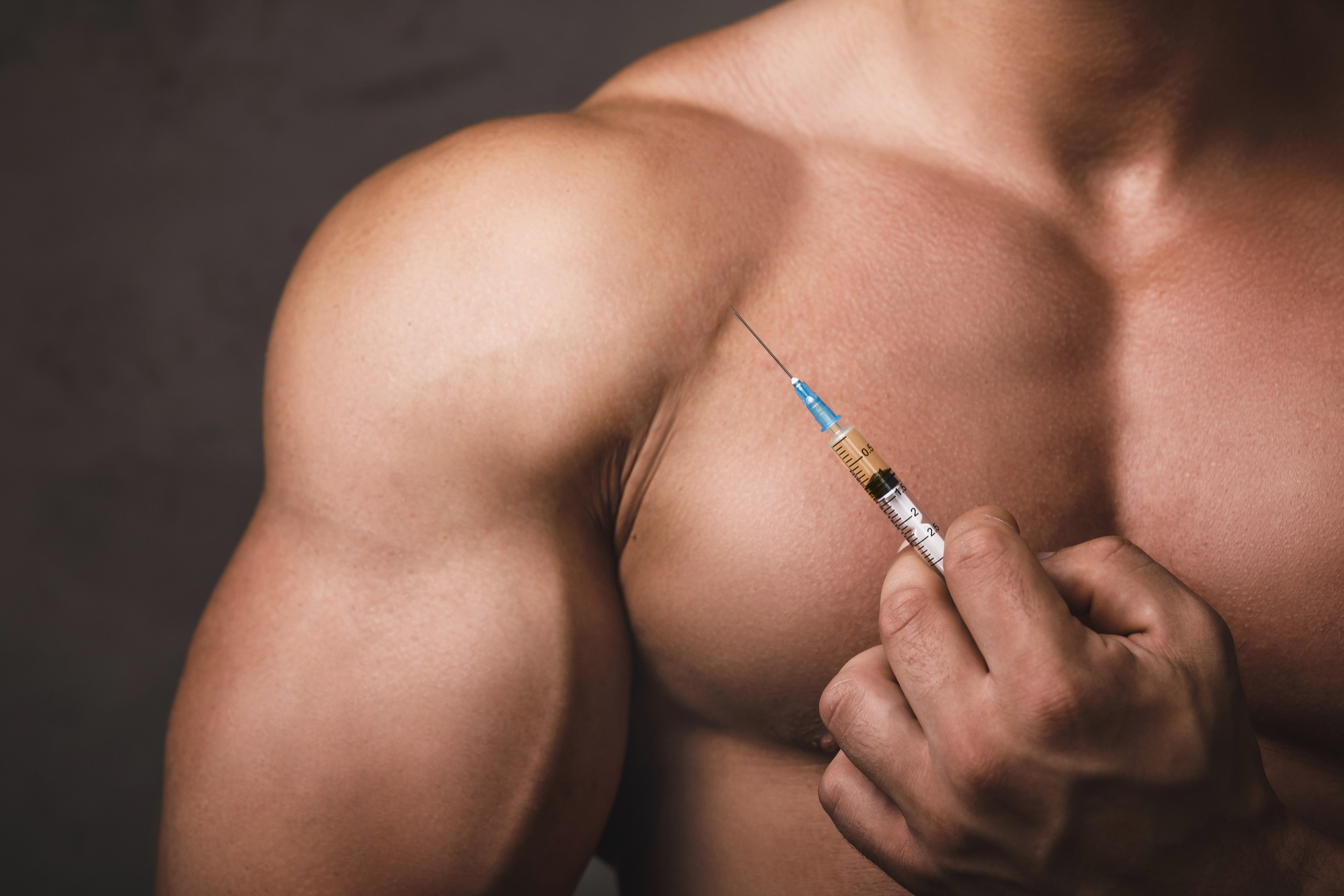 Muscular man holding steroid injection in front of shoulder